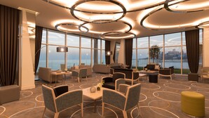 Eine moderne Hotelhalle mit einer großen Sitzgruppe, einem Esstisch und Blick aufs Meer.
