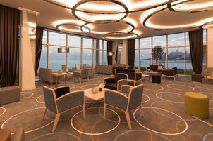 Un moderno vestíbulo de hotel con una amplia zona de estar, una mesa de comedor y vistas al mar.