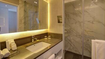 Un baño moderno con lavamanos de mármol, cabina de ducha de vidrio y un espejo grande.