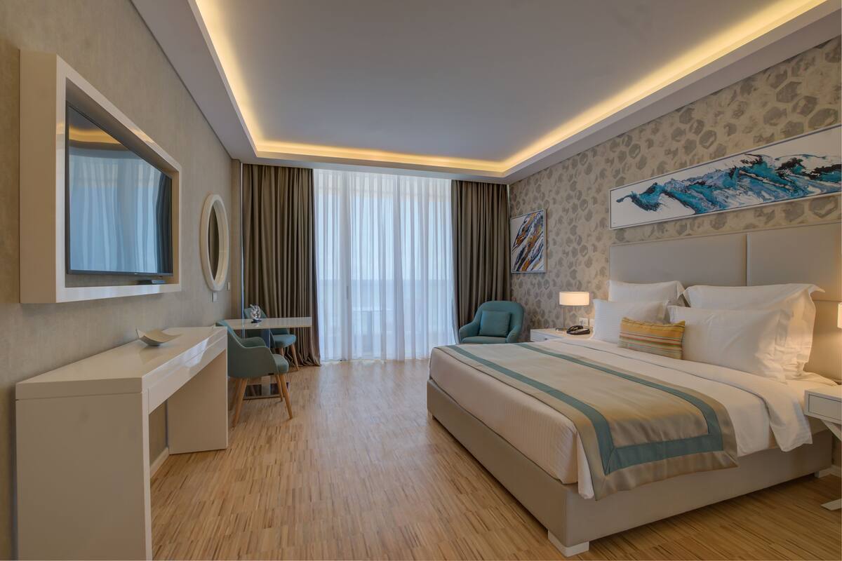 A hotel room with a bed, desk, chair, and a large window with curtains.