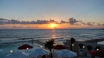 Een zonsondergang uitzicht vanaf een hotel aan het strand, met parasols en ligstoelen.