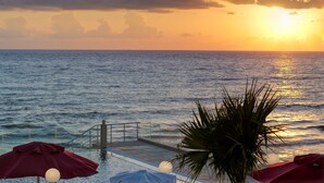 Ein Sonnenuntergangsblick von einem Poolbereich mit Geländer und Sonnenschirmen.