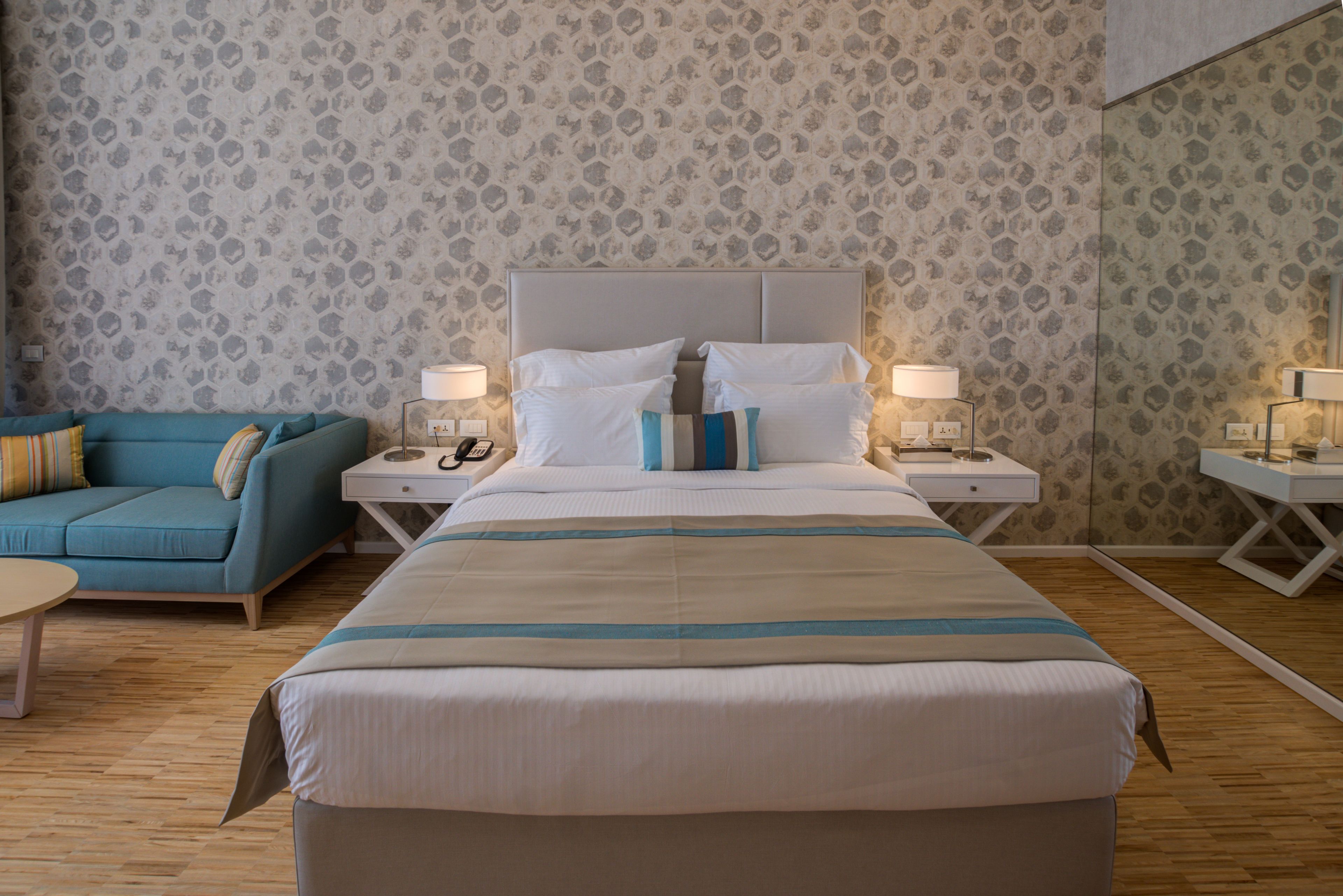 A hotel room with a large bed, a sofa, two bedside tables with lamps, and patterned wallpaper.