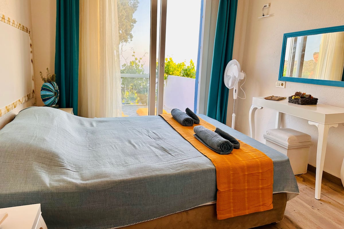 A hotel room with a bed, a desk, a mirror, and a view of the outdoors.