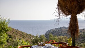 A table set for four with a checkered tablecloth, plates, cutlery, and a candle holder, overlooking a coastal landscape with hills and the sea. - Goknar Knidos Nature Hotel and Farm (Datça)