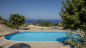A clear blue swimming pool with lounge chairs and umbrellas, surrounded by trees and a view of the sea. - Goknar Knidos Nature Hotel and Farm (Datça)