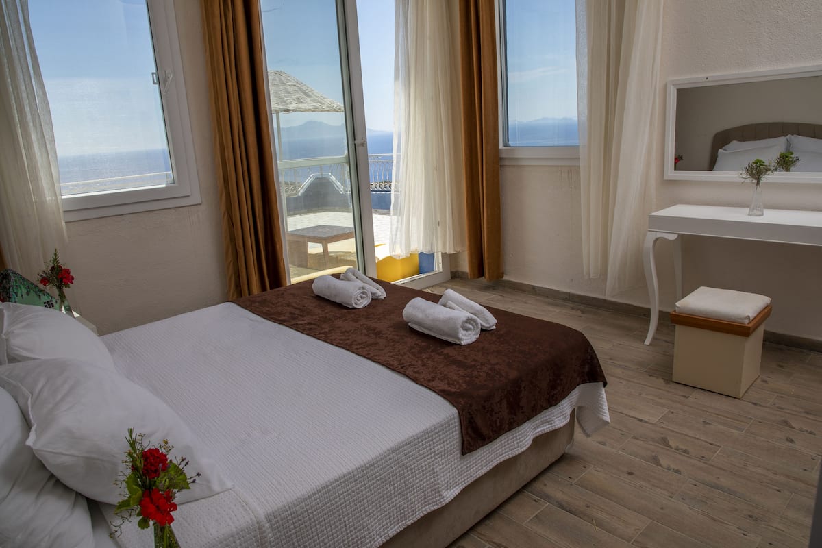 A hotel room with a bed, a desk, a chair, and a view of the sea.