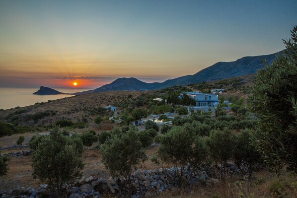 A coastal landscape with a sunset, a hill with sparse vegetation, and a modern house with multiple rooms. - Goknar Knidos Nature Hotel and Farm (Datça)