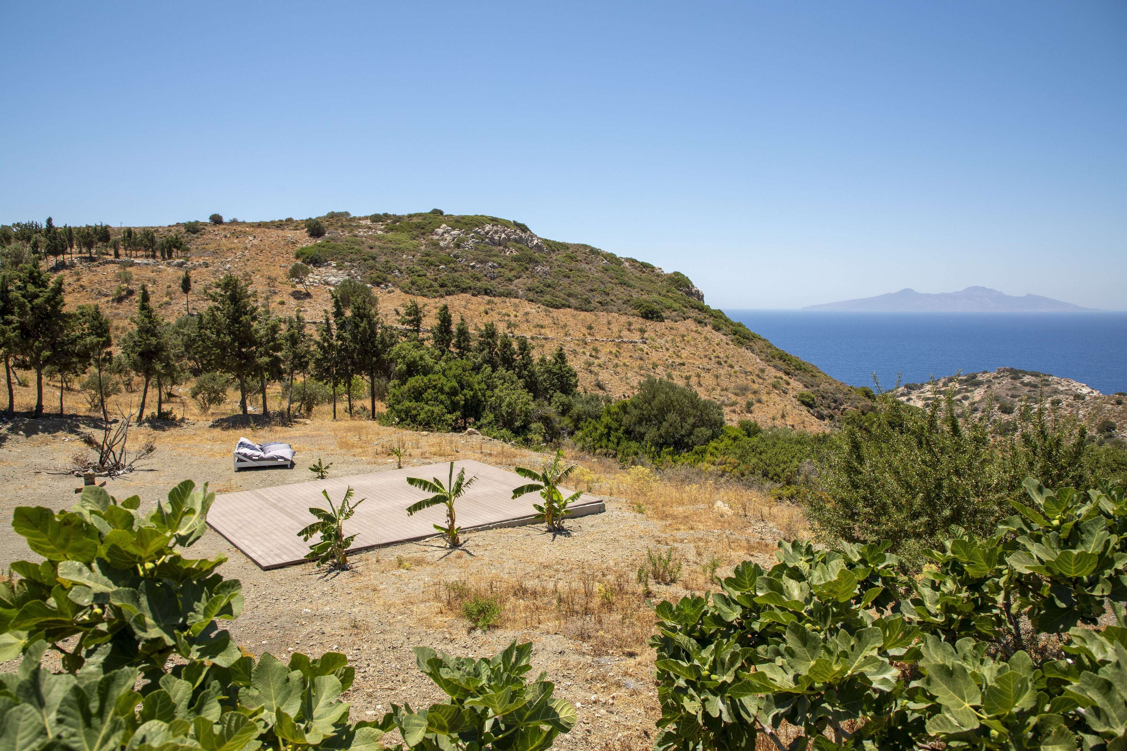 A hillside with a clear view of the sea, a small table, and some trees.
