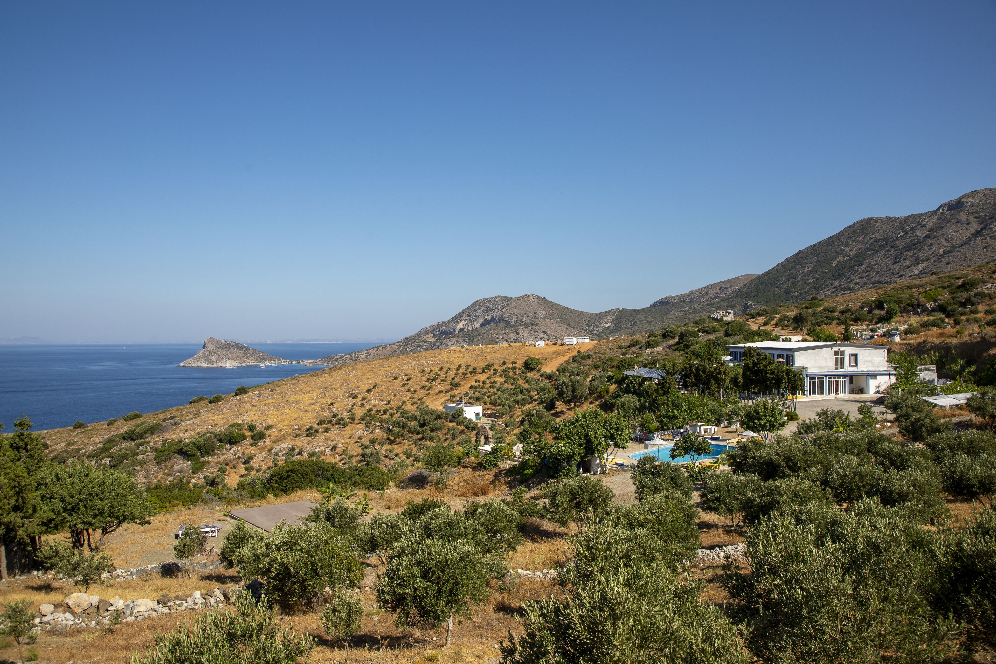 A coastal property with a swimming pool, a large house, and a view of the sea and hills.