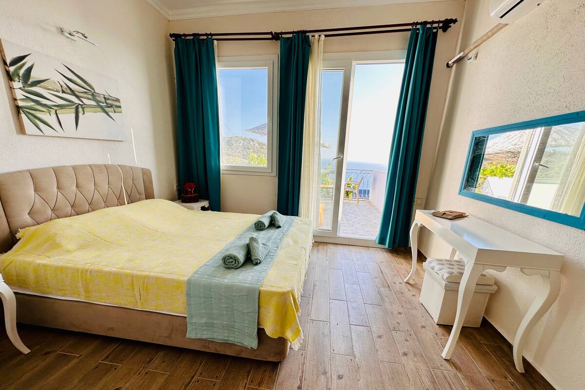 A bedroom with a bed, a desk, and a view of the sea.