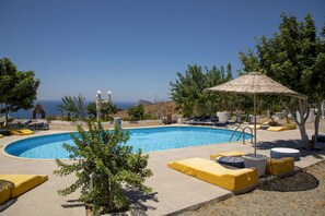 A swimming pool with lounge chairs and a shaded area, surrounded by trees and a view of the sea. - Goknar Knidos Nature Hotel and Farm (Datça)