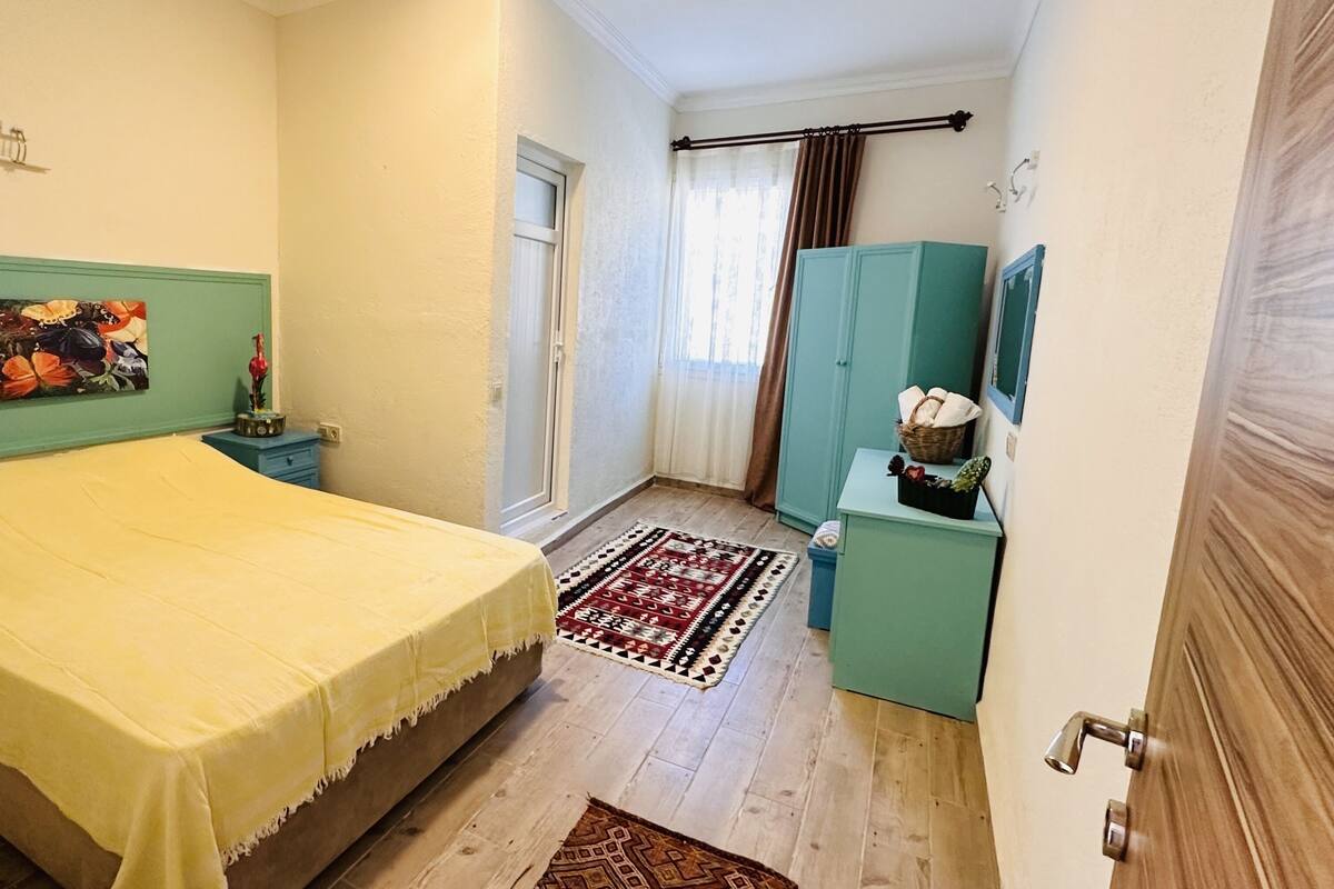 A bedroom with a bed, a nightstand, a dresser, a window with curtains, and a door.