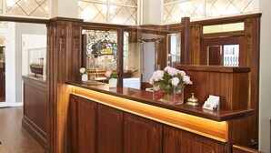 A reception desk with a wooden finish, a stained glass window, and a vase with flowers. - Hotel Cap Polonio Pinneberg (Pinneberg)