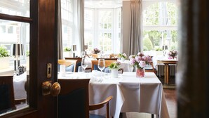 A dining area with tables set for service, large windows, and a view of greenery outside. - Hotel Cap Polonio Pinneberg (Pinneberg)