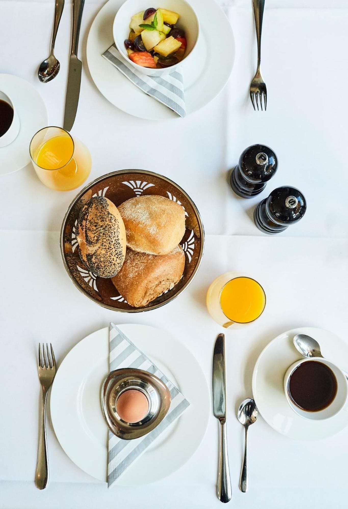 A breakfast setting with a plate of bread, a bowl of fruit, and a cup of coffee.