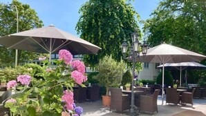 An outdoor seating area with umbrellas, potted plants, and outdoor furniture. - Hotel Cap Polonio Pinneberg (Pinneberg)