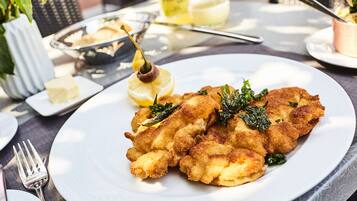 Un plato de comida rebozada y frita con una cuña de limón y verduras, servido en un plato blanco.