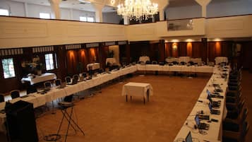 Un amplio salón de conferencias con varias mesas y sillas, una araña de cristal y suelo alfombrado.
