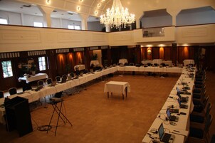 Un amplio salón de conferencias con varias mesas y sillas, una araña de cristal y suelo alfombrado.