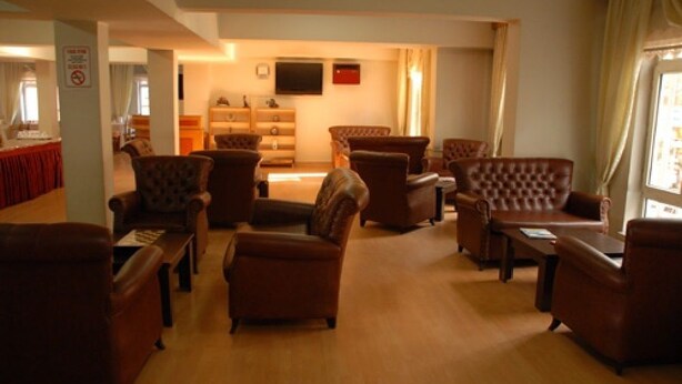 A spacious living room with leather sofas and armchairs arranged around a central coffee table. A flat-screen TV is mounted on the wall, and a fireplace is visible in the background. - Otel Akkoc (Isparta)