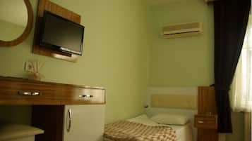 Un dormitorio con una cama, un televisor montado en la pared, una mesita de noche pequeña y un equipo de aire acondicionado.