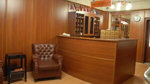 A reception area with a wooden reception desk, a leather chair, and a bookshelf filled with flags. - Otel Akkoc (Isparta)