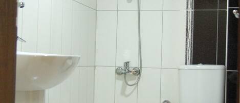 Ein kleines, sauberes Badezimmer mit weißen Fliesen, einem weißen Waschbecken, einer Toilette und einer Dusche mit Glaswand.
