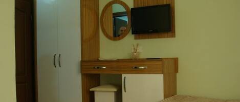 Una habitación con cama, escritorio, armario, televisor y espejo.