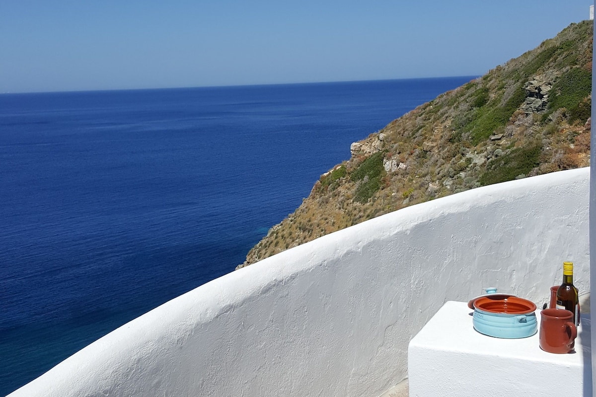 A white-walled building with a view of the sea and a distant airplane.