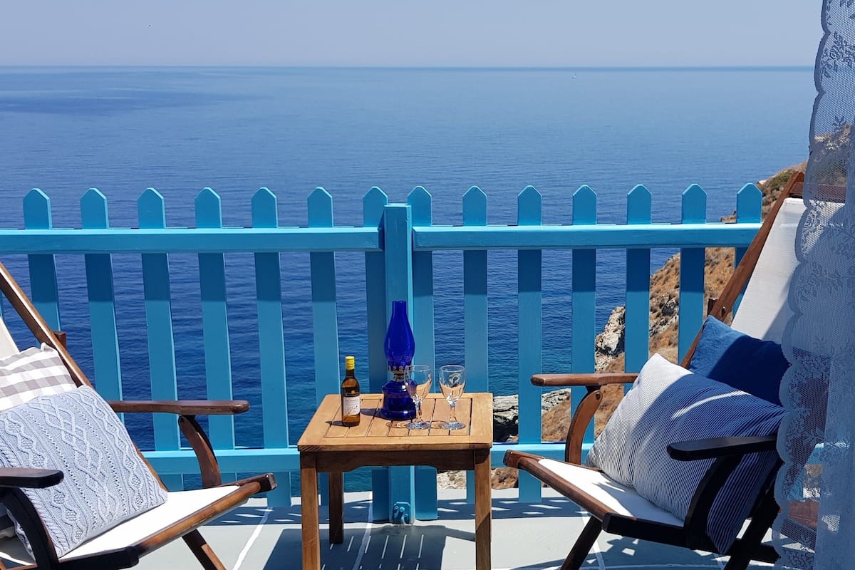 A balcony with two wooden chairs, a small table with a bottle and glasses, and a view of the sea.