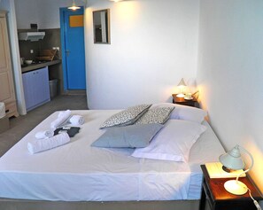 A neatly made bed with towels and pillows, a bedside lamp, and a small table with a book. - Aegean Eye Apartments (Sifnos)
