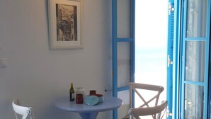 Une pièce avec une table ronde et deux chaises blanches  à assise tressée, un tableau encadré au mur et une porte bleue donnant sur l’extérieur.