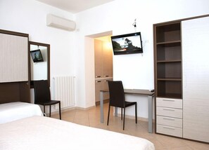 A hotel room with a bed, a desk, two chairs, a TV, and a wardrobe. - Il Nespolo Fiorito (Orosei)