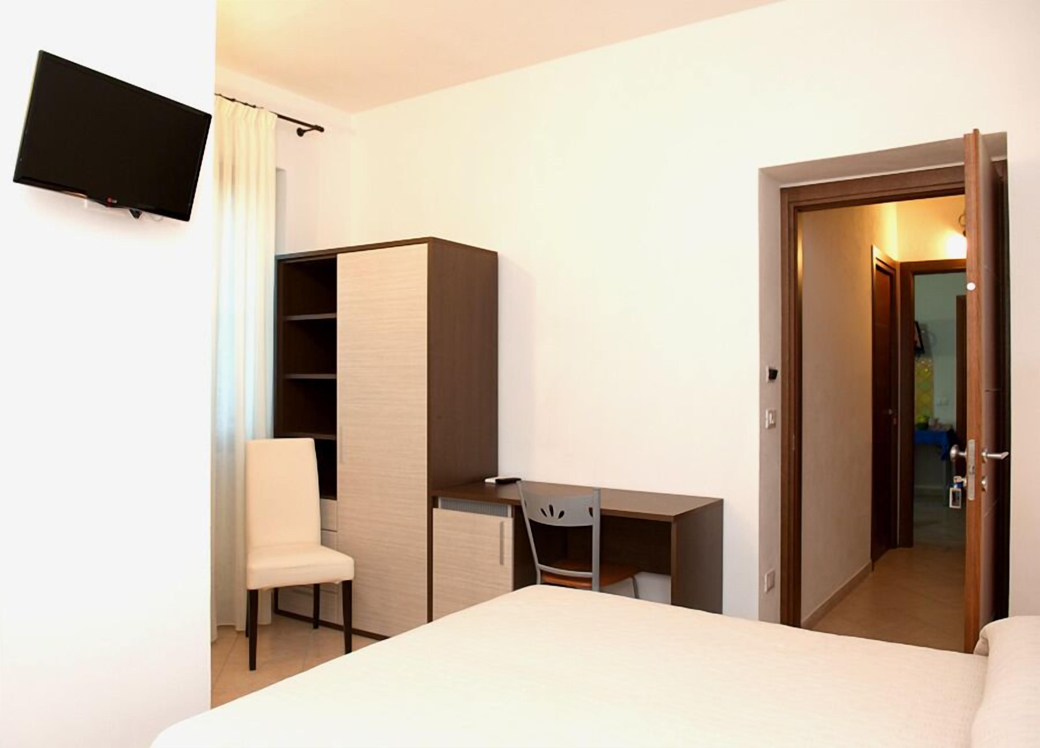 A hotel room with a bed, a desk, a chair, a wardrobe, and a television on the wall.