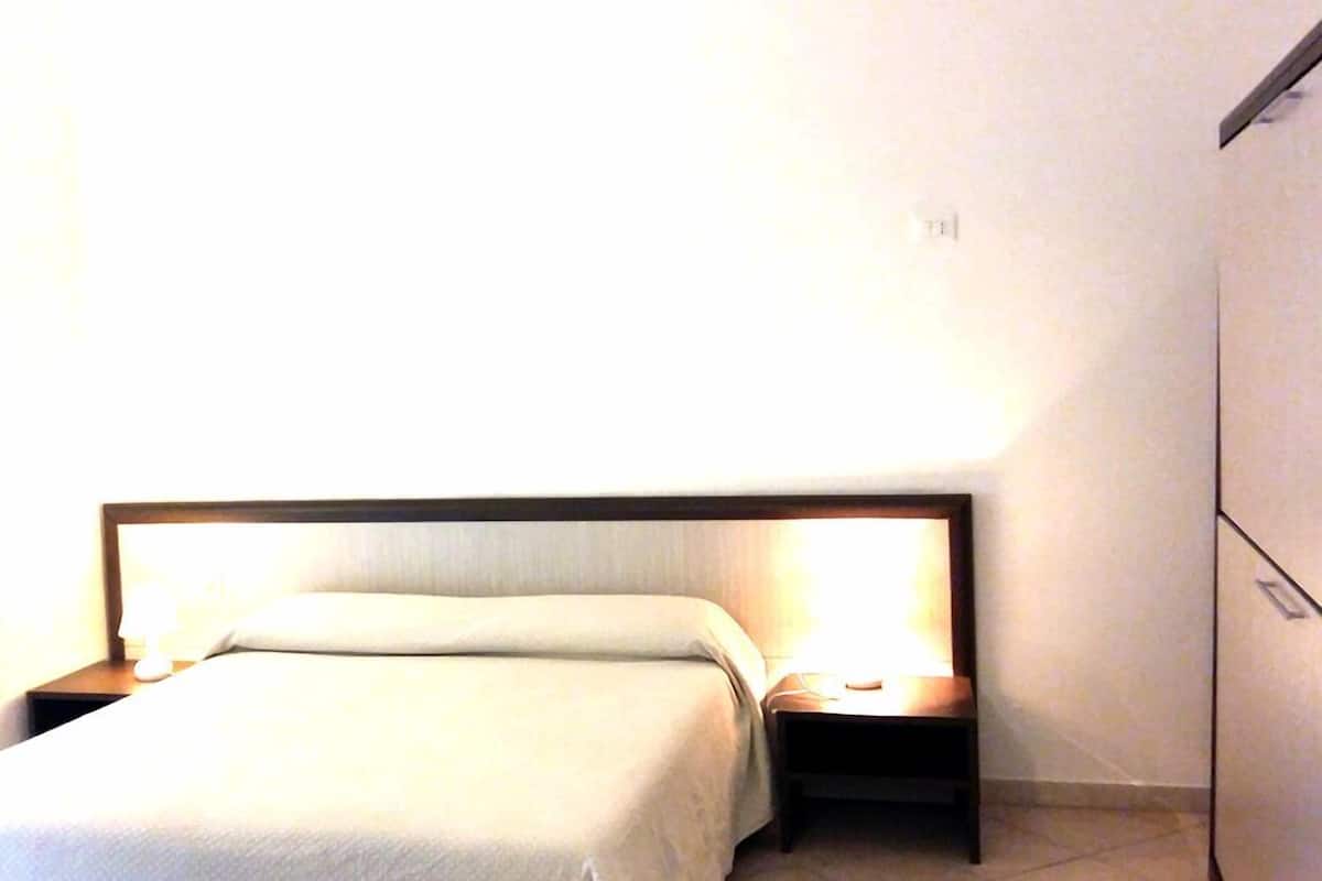 Een netjes opgemaakt bed met een houten hoofdbord en twee nachtkastjes, elk met een lamp.