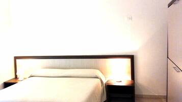 Un letto ben rifatto con una testiera in legno e due comodini, ognuno con una lampada.