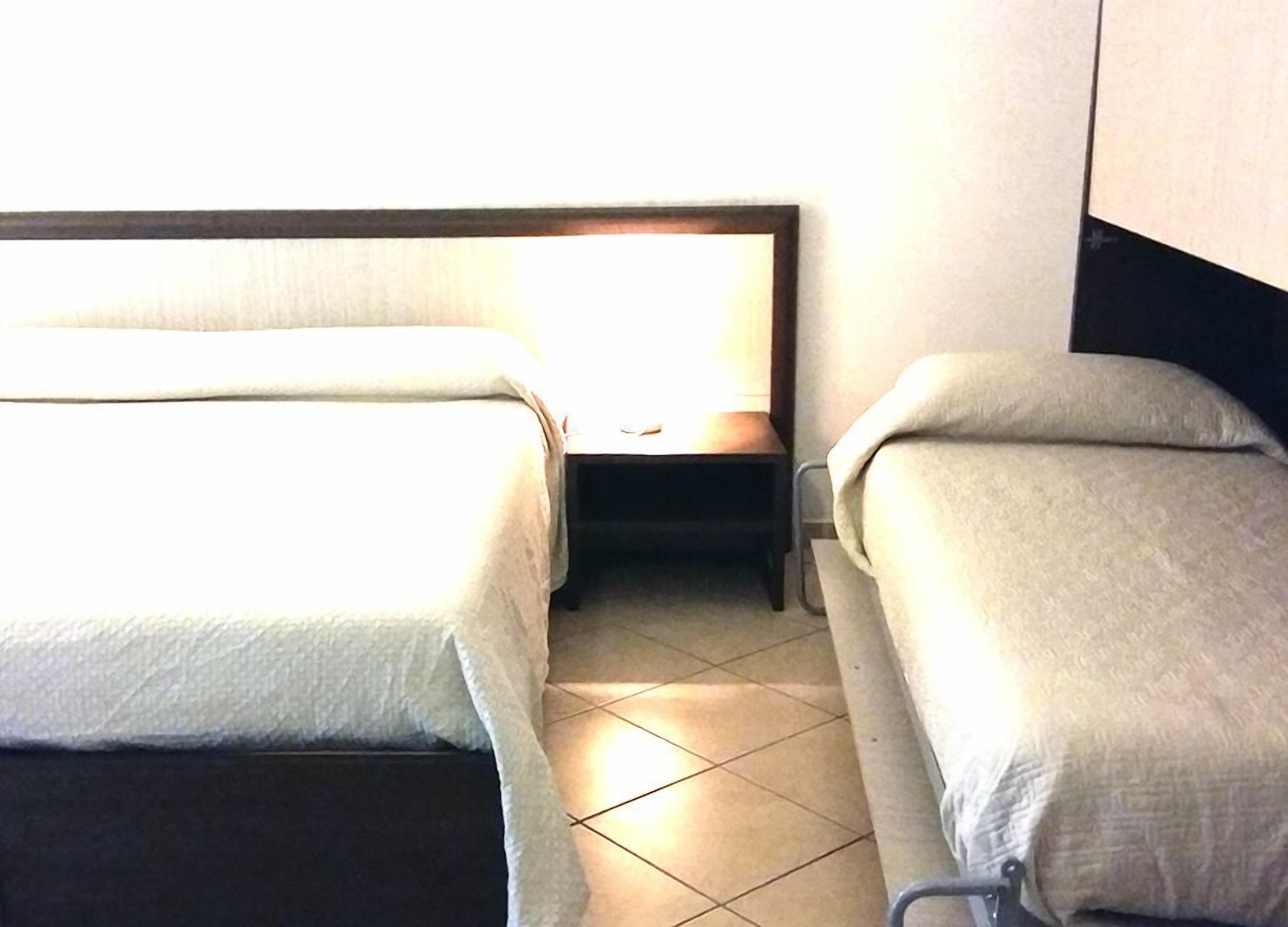 Ett hotellrum med två separata sängar, ett nattduksbord och en vägglampa.