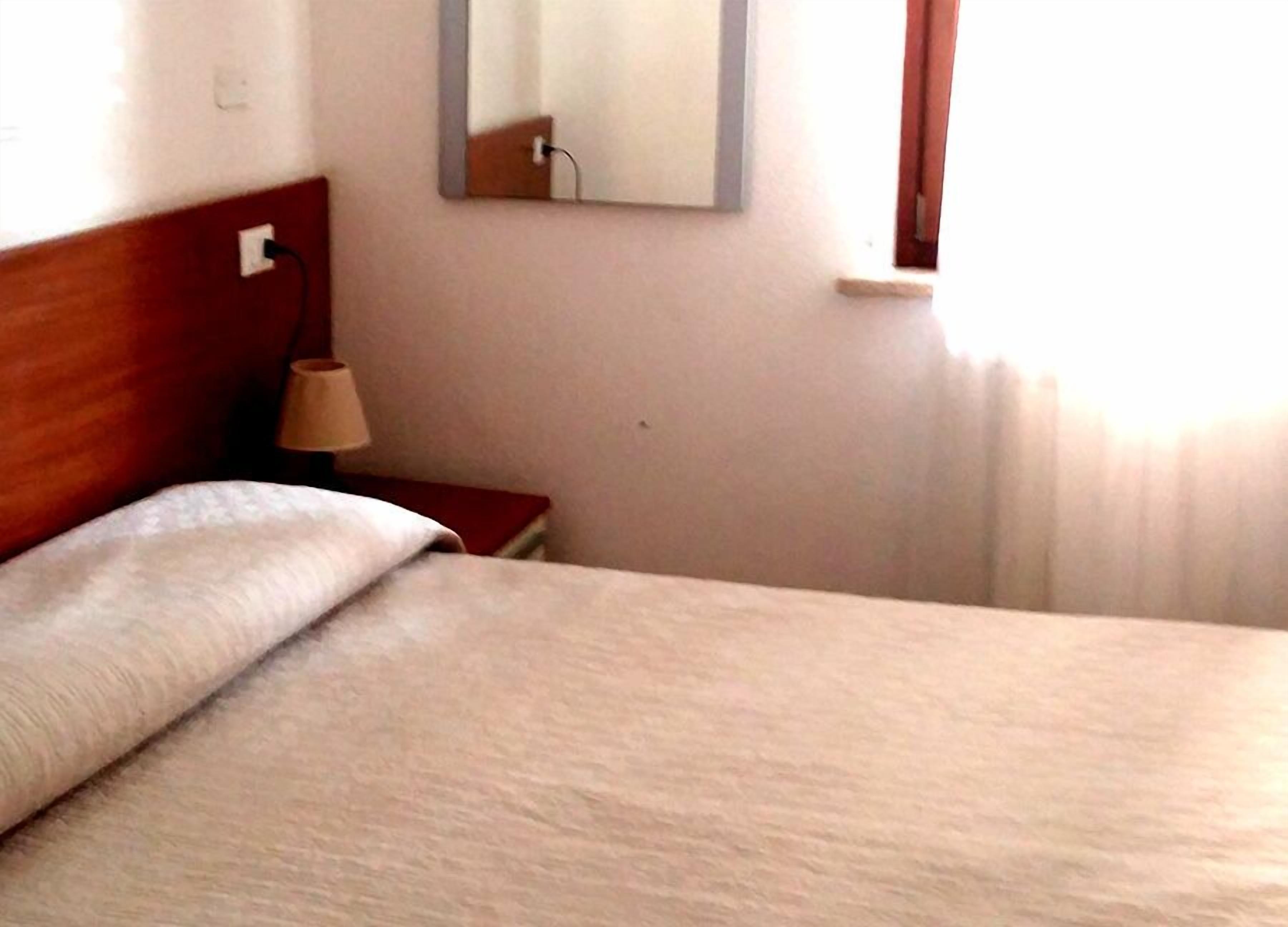 A neatly made bed with a wooden headboard, a bedside lamp, and a mirror on the wall.