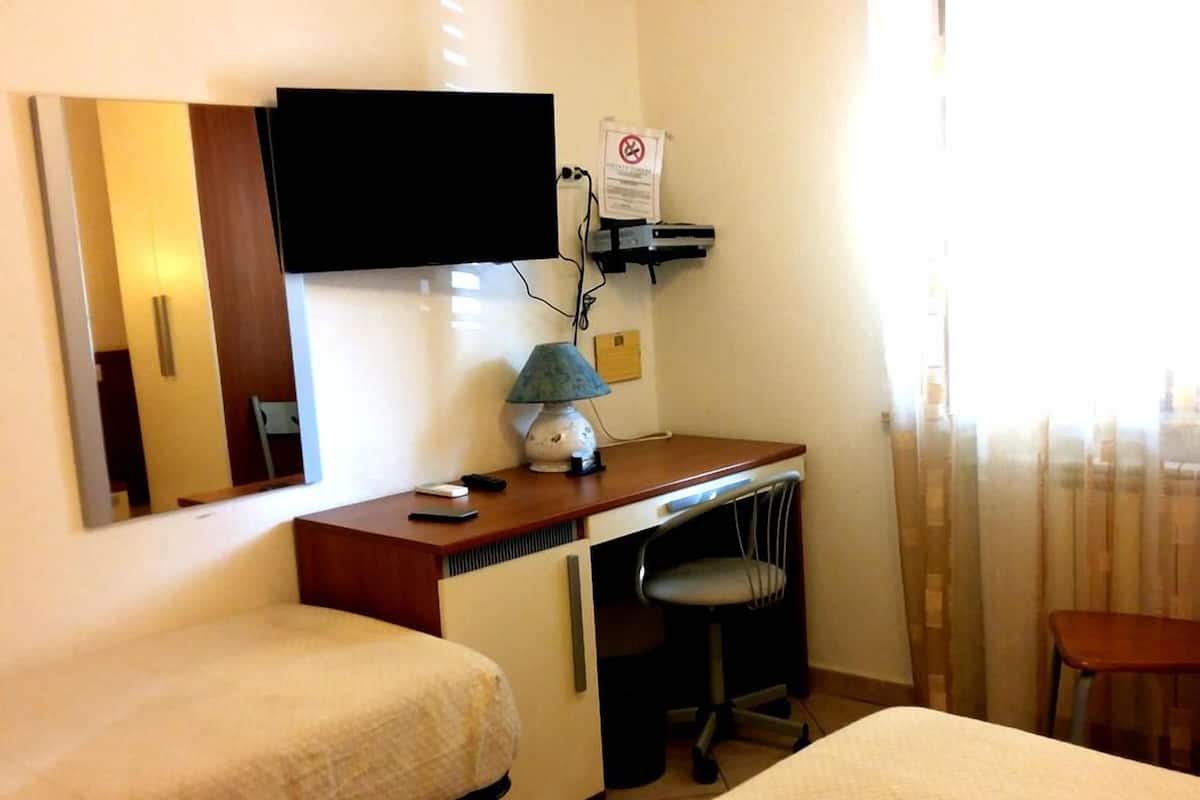 Een hotelkamer met een bed, een bureau met stoel, een aan de muur bevestigde televisie en een raam met gordijnen.