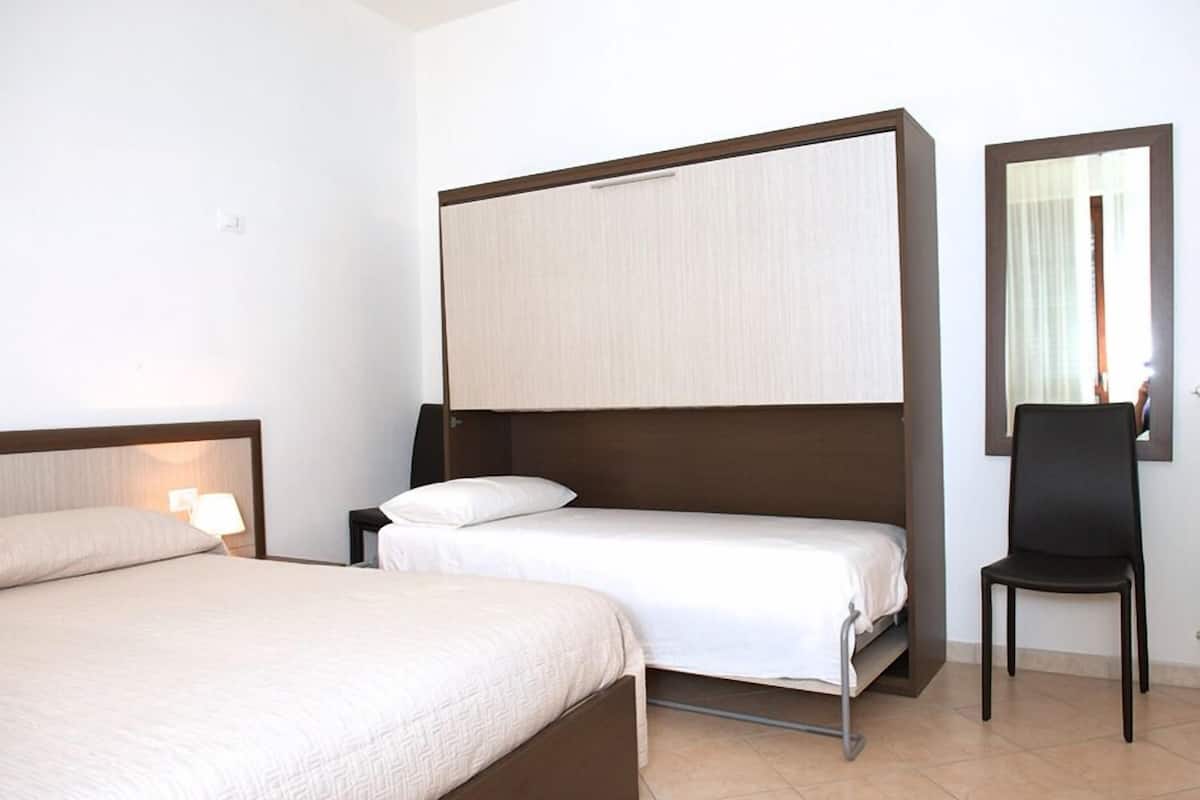 Een hotelkamer met een tweepersoonsbed, een eenpersoonsbed, een stoel, een nachtkastje en een spiegel.