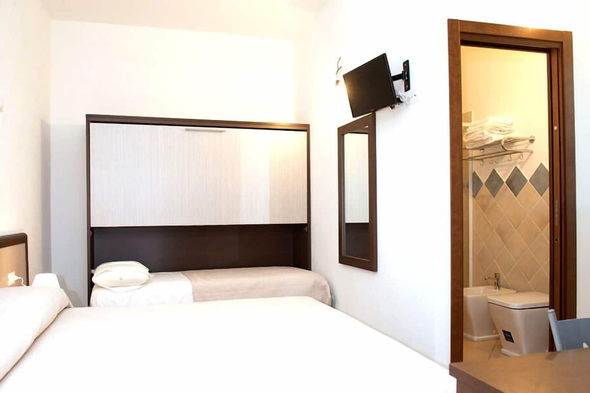 Hotelkamer met een bed, een aan de muur bevestigde televisie, een badkamer met wastafel en toilet, en een spiegel.