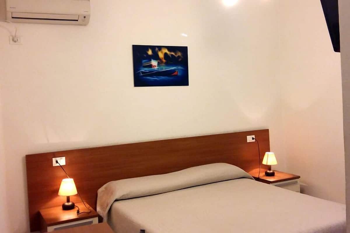 Een hotelkamer met een bed, twee bedlampen, een airconditioner en een schilderij aan de muur.