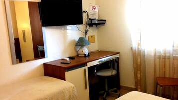Une chambre d’hôtel avec deux lits simples, un bureau avec une lampe, un téléviseur fixé au mur et une chaise.