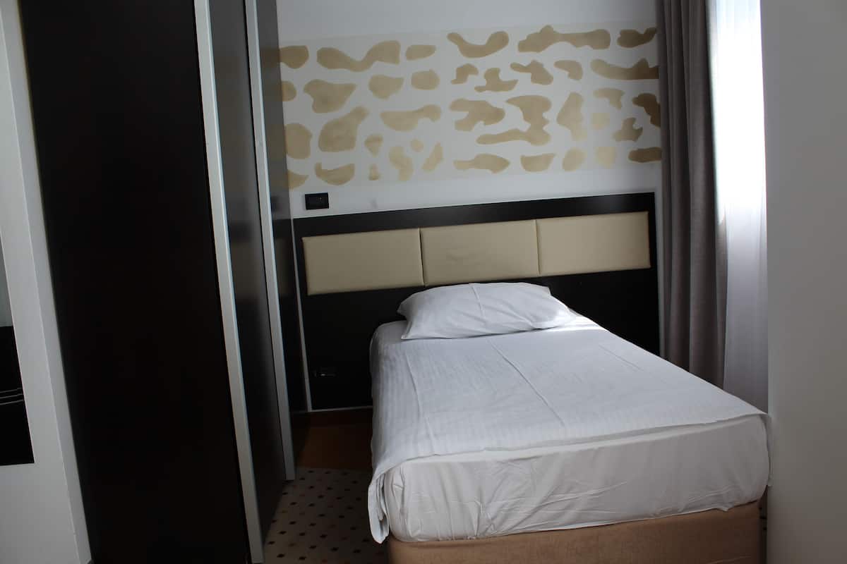 A hotel room with a bed, a headboard, and a patterned wall.