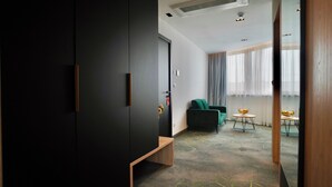 A modern hotel room with a dark wardrobe, a green sofa, a small round table with fruit, and a view of the outdoors through large windows. - Hotel Diplomat (Zagreb)