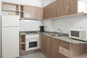 Una cocina con armarios de madera, un refrigerador blanco, una estufa, un microondas y un fregadero.
