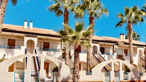 A hotel with multiple floors, palm trees, and a clear blue sky. - Destinos de Sol Los Alcázares (Los Alcazares)