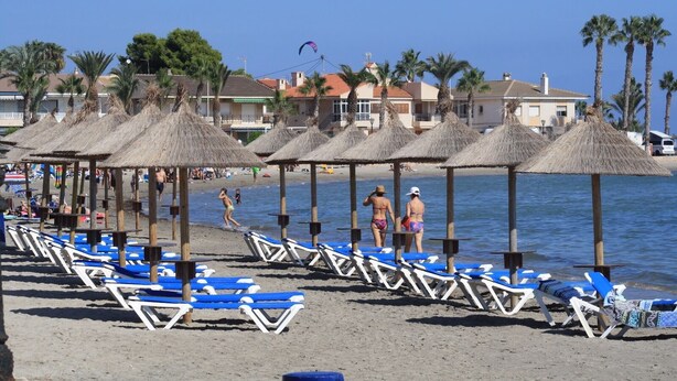 A beach with rows of blue and white lounge chairs, thatched umbrellas, and palm trees. - Destinos de Sol Los Alcázares (Los Alcazares)
