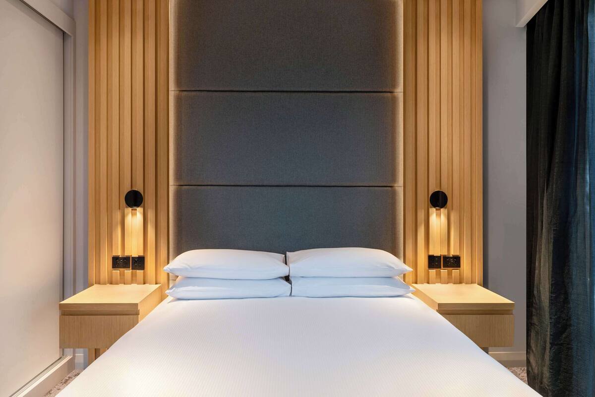 Een moderne hotelkamer met een groot bed, houten paneelwanden en twee bedlampjes.